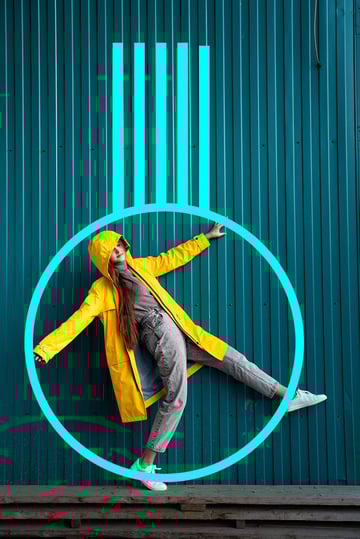 A girl in jeans and a yellow raincoat stands on one leg.