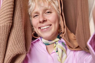 Blonde woman exudes positivity confidence as stands amidst delightful assortment of clothes on