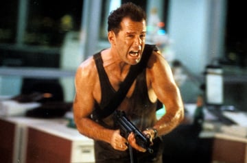 McClane with a large gun running through an office