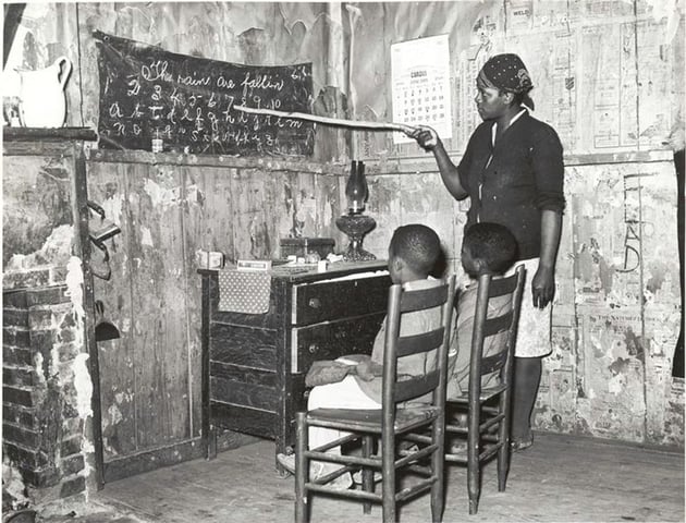 Mother teaching children numbers and alphabet in sharecropper's home, Louisiana. Source: Schomburg Center for Research in Black Culture