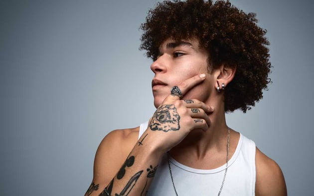 Serious young tattooed black man touching chin in gray studio