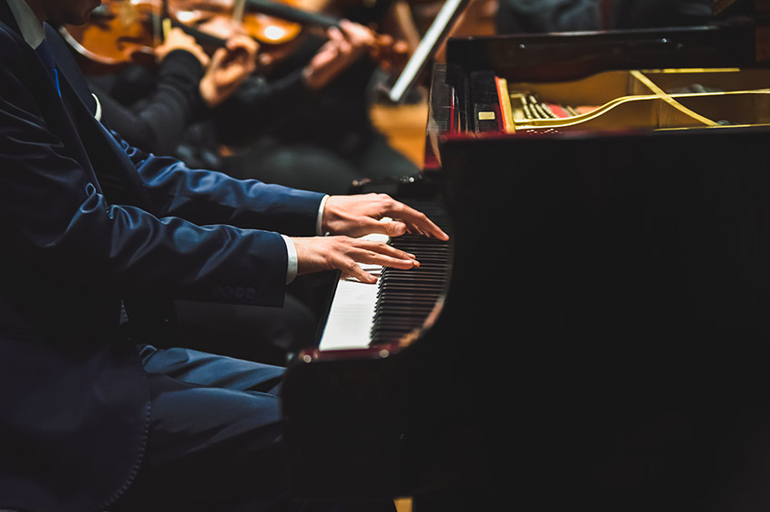 Pianist playing a piece on a grand piano at a concert, seen from the side