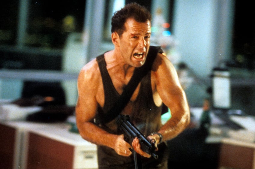 McClane with a large gun running through an office