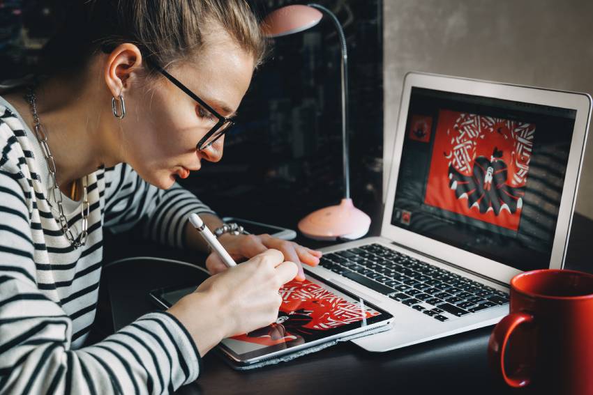 Young beautiful in glasses drawing on IPad tablet with latest pencil on photoshop